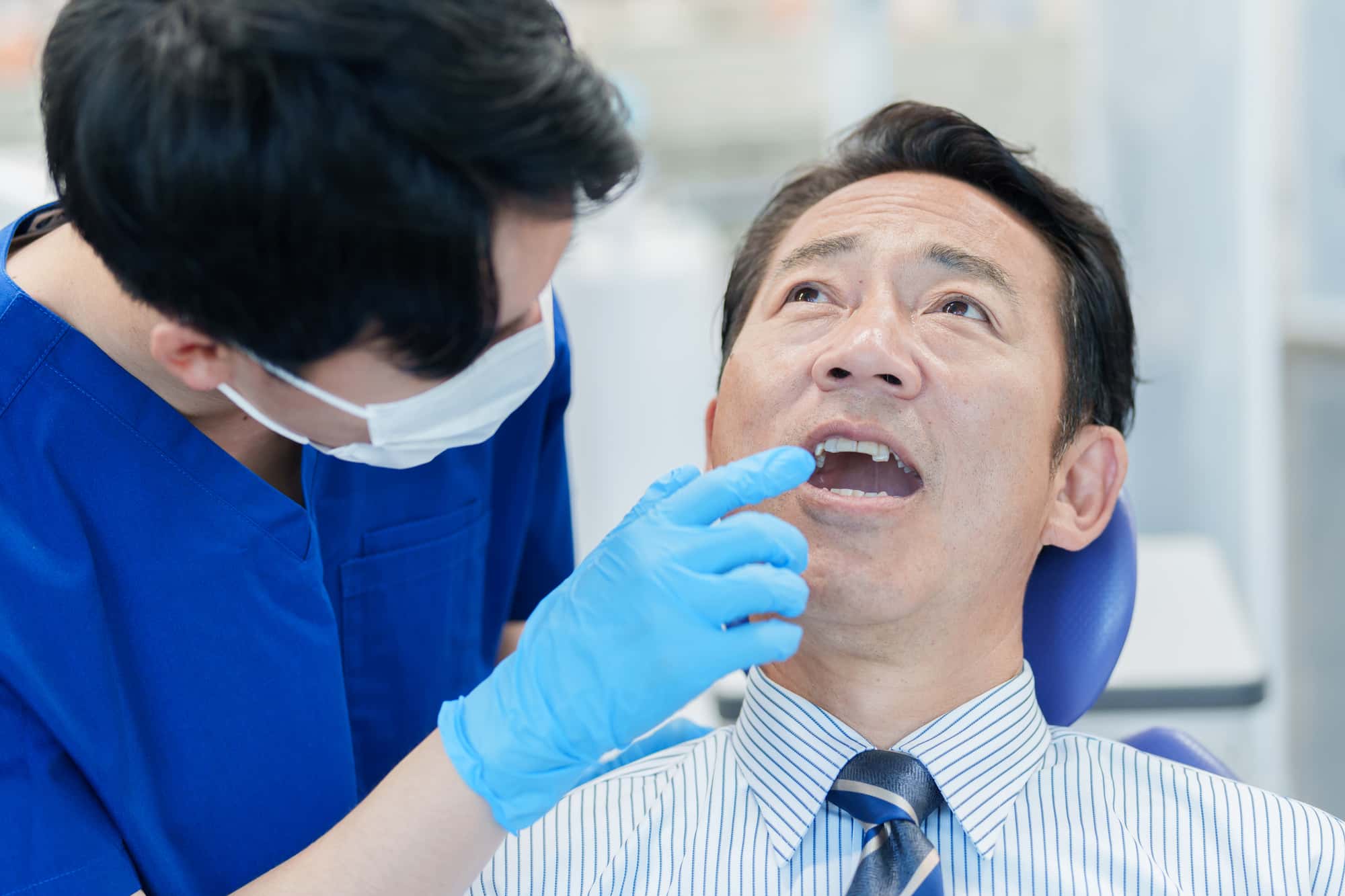 インプラントの保証を受けるために歯科医に定期メンテナンスをしてもらう男性
